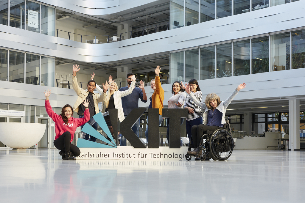 Gruppe von Menschen jubelt vor dem Logo des Karlsruher Instituts für Technologie in einem Gebäude.